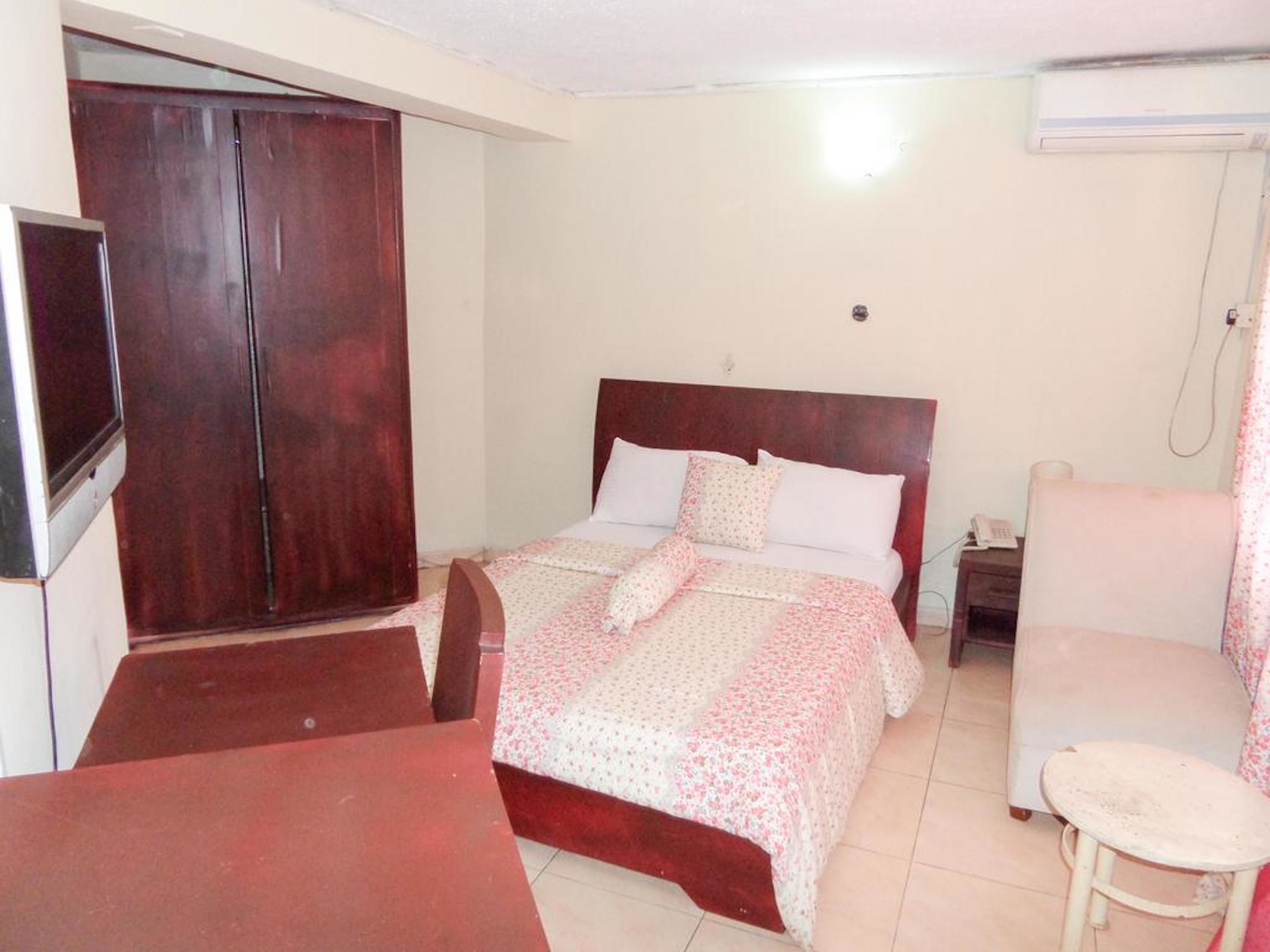 Una camera d'albergo con un letto, una scrivania, una sedia, un armadio e un condizionatore.