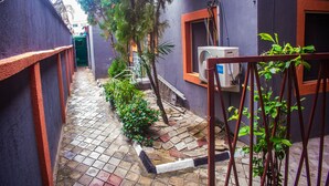 A narrow alleyway with a tiled floor, surrounded by buildings with purple and red walls. There is a small garden with plants and a tree. - Peerage Retreat and Resort (Lagos)