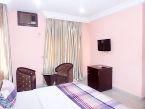 A hotel room with a bed, a desk, a chair, a television, and curtains. - New Golden Hotel (Abuja)