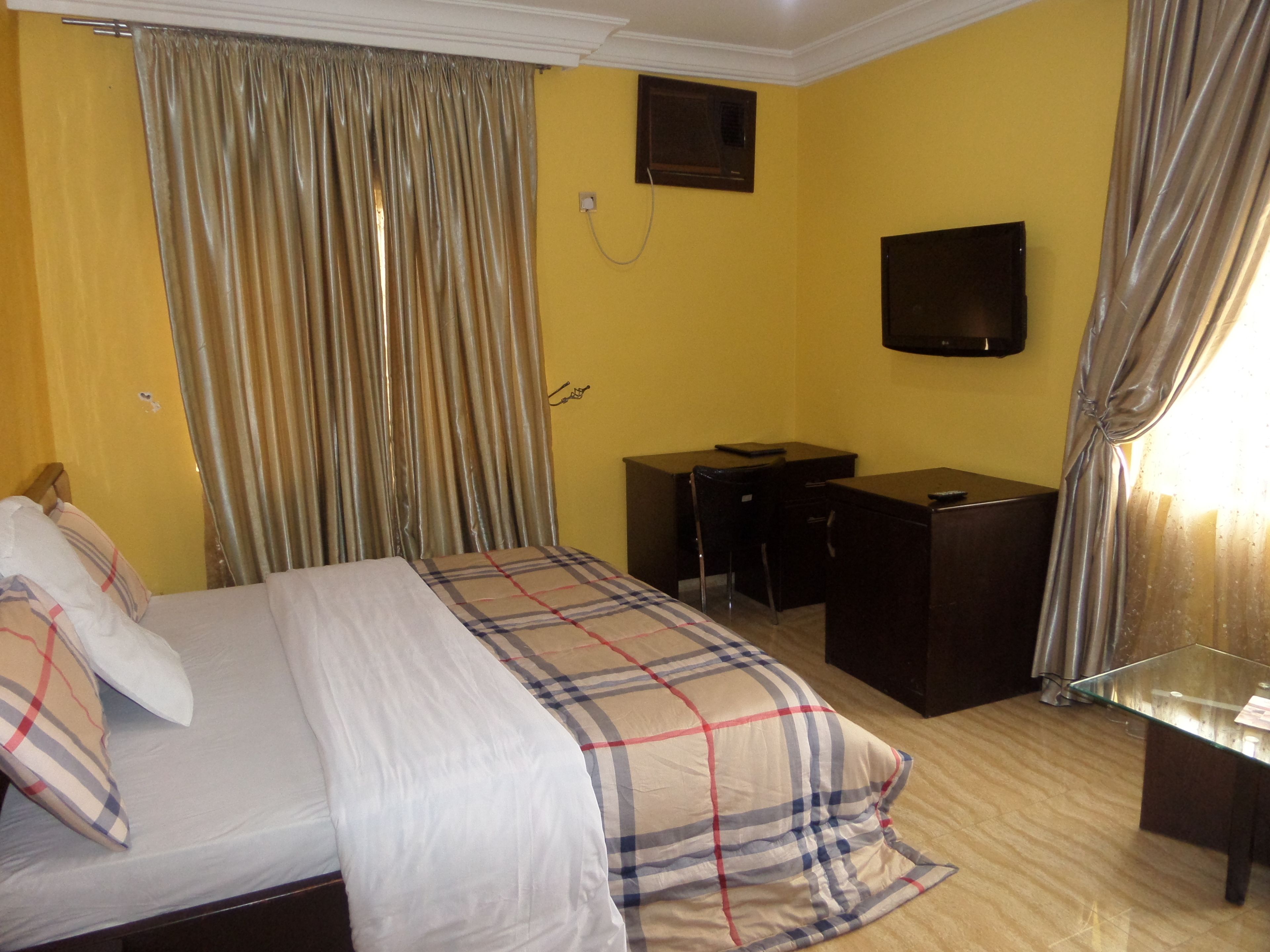Una habitación de hotel con cama, escritorio, televisor y cortinas.