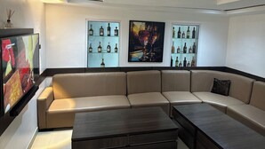 A modern living room with a beige sectional sofa, a dark wooden coffee table, and two wall-mounted shelves displaying bottles. - Foramot Suite (Lagos)