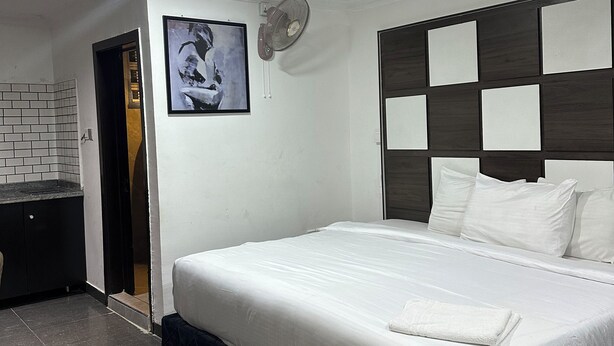 A modern bedroom with a large bed, a built-in desk, and a ceiling fan. - Foramot Suite (Lagos)
