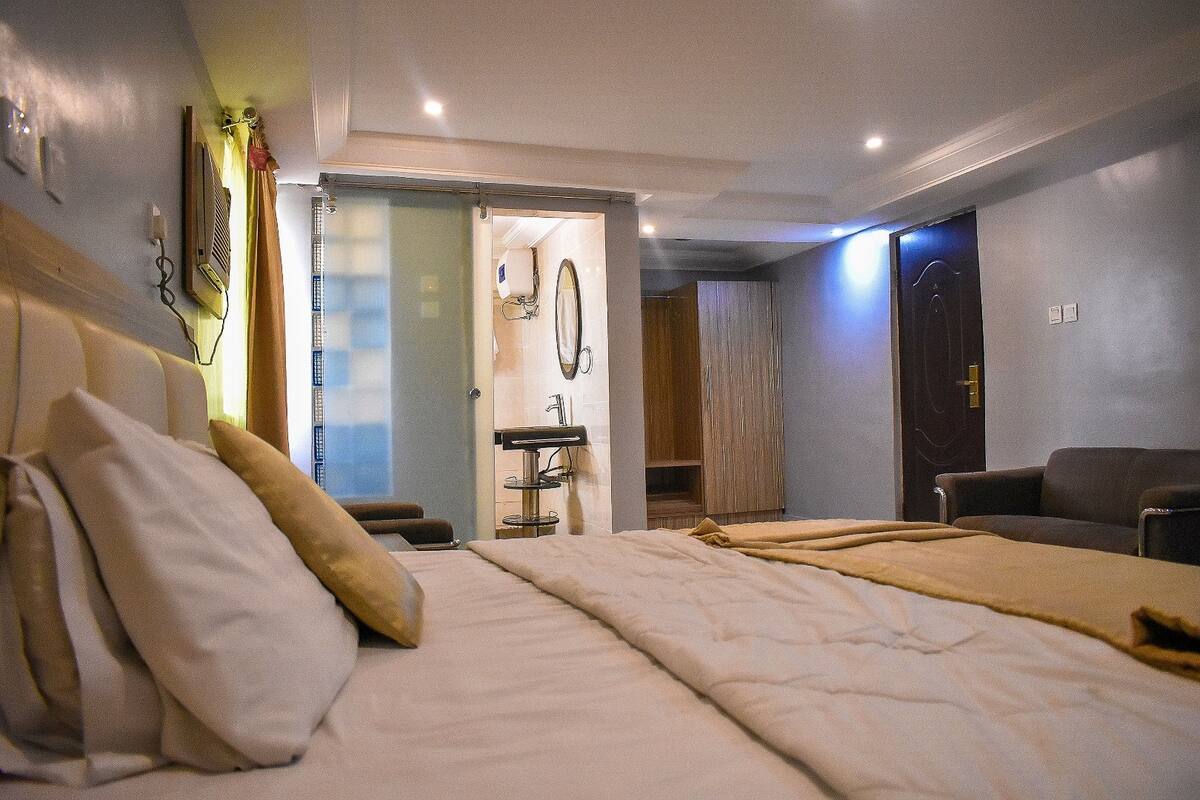 A hotel room with a bed, a chair, a desk, a mirror, and a bathroom visible through an open door.
