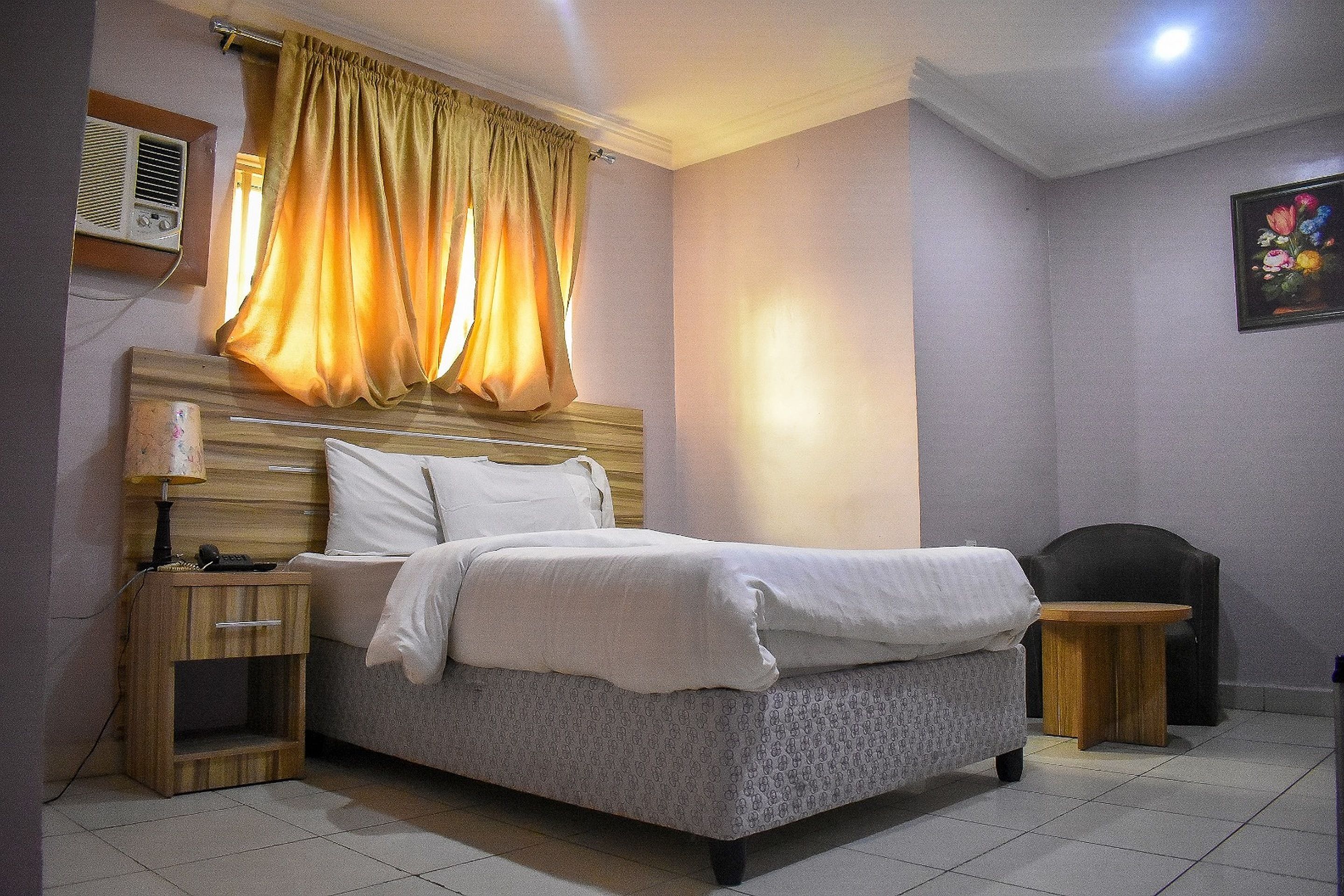 A bedroom with a bed, bedside tables, a lamp, an air conditioner, and a curtain.