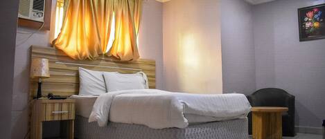 A bedroom with a bed, bedside tables, a lamp, an air conditioner, and a curtain.