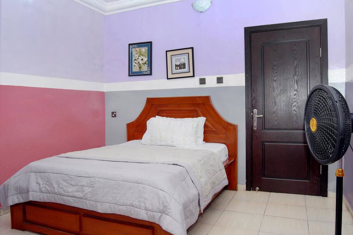 Un dormitorio con cama de madera, una puerta oscura y un ventilador fijado a la pared.