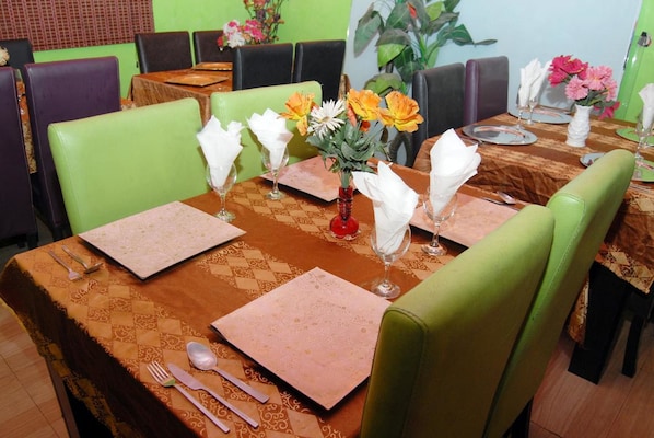 A restaurant dining area with tables set for four, each with a brown tablecloth, white napkins, and a vase of flowers.