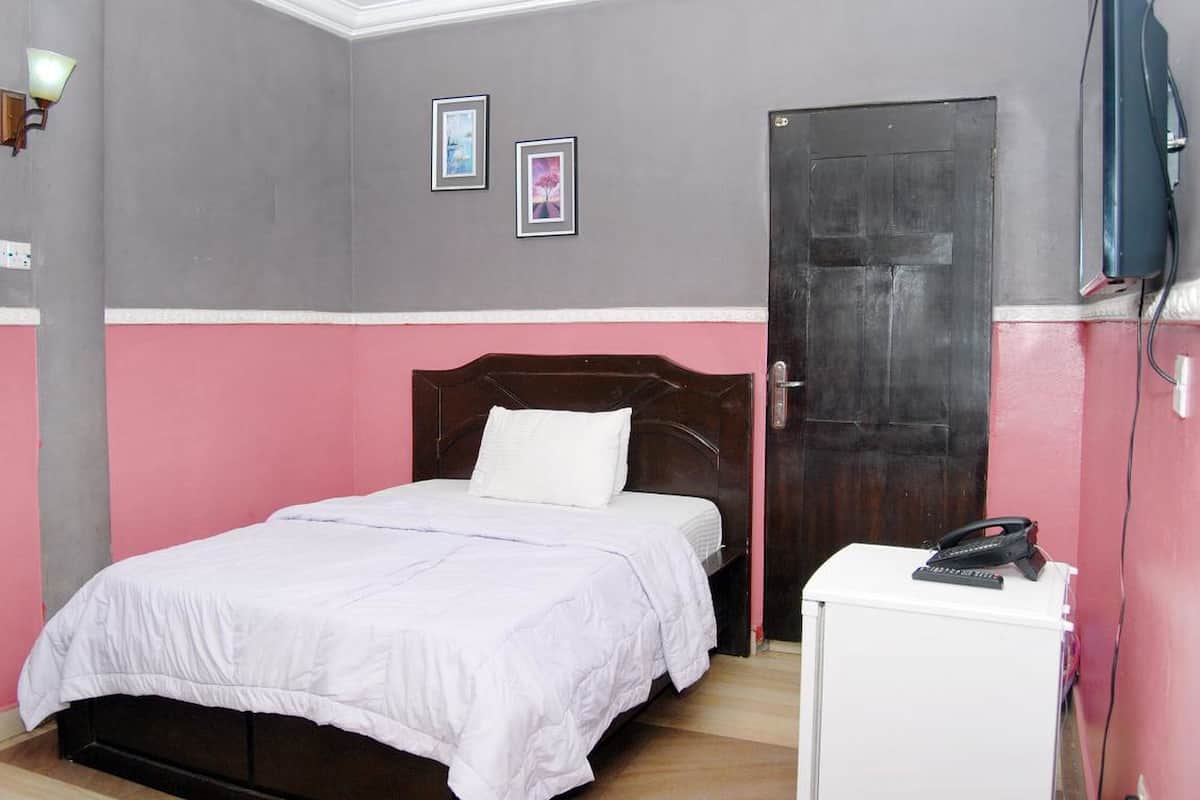 Un dormitorio con una cama, una puerta, un armario blanco pequeño y dos cuadros en la pared.