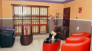 A lobby with a reception desk, a brown leather sofa, a red sofa, and a black leather chair. - Royal Park Hotel & Suites (Lekki)