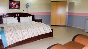 A bedroom with a bed, a nightstand, a wardrobe, and a chair. - Royal Park Hotel & Suites (Lekki)