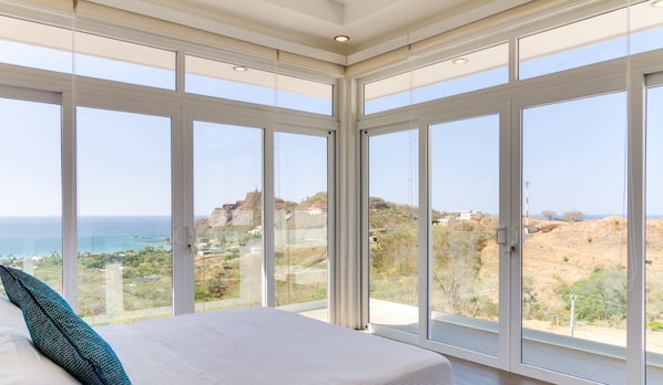 A bedroom with a large bed, a view of the sea, and a mountainous landscape.