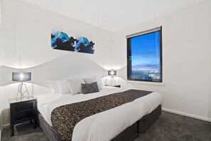 A modern hotel room with a large bed, two bedside tables, a city view window, and abstract wall art. - Premier stays (Southbank)