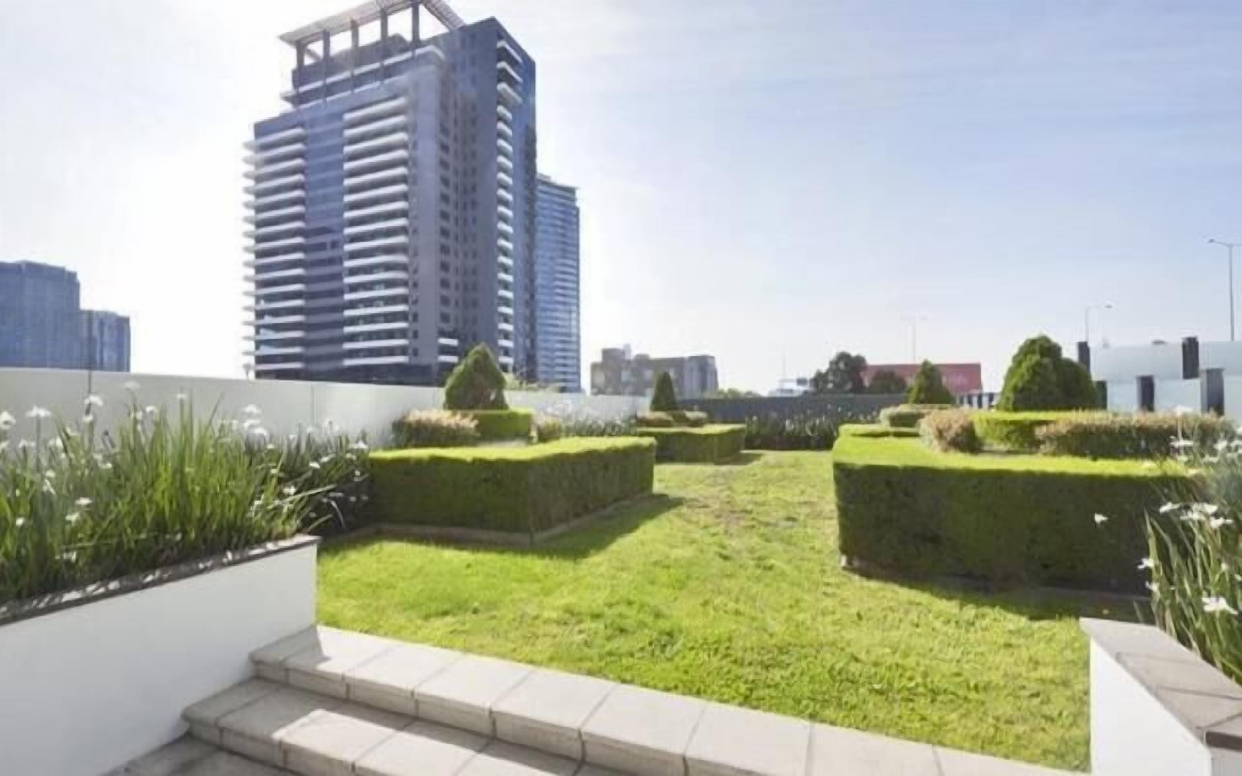 A rooftop garden with neatly trimmed grass and hedges, surrounded by modern buildings.