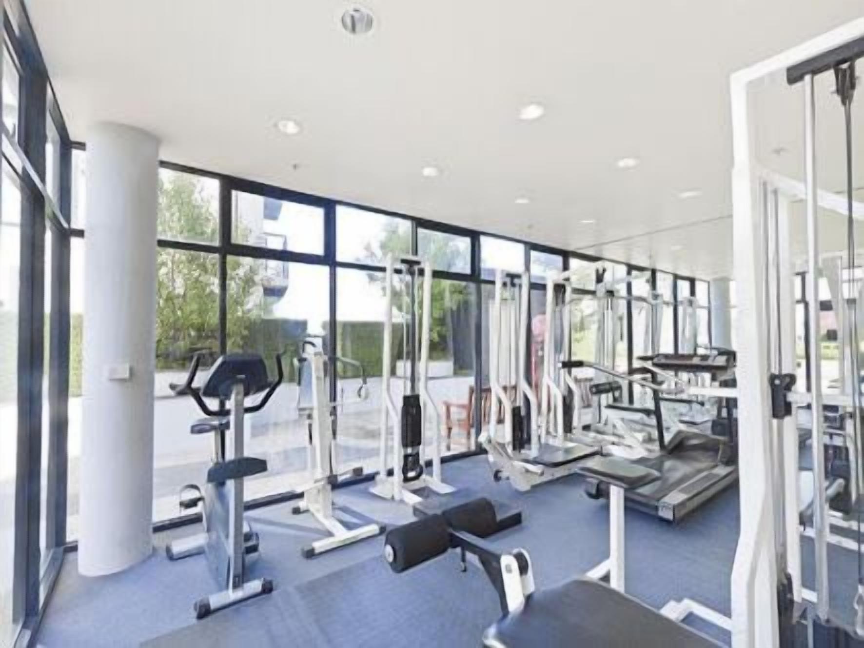 A modern gym with various exercise equipment, large windows, and a clean, spacious layout.