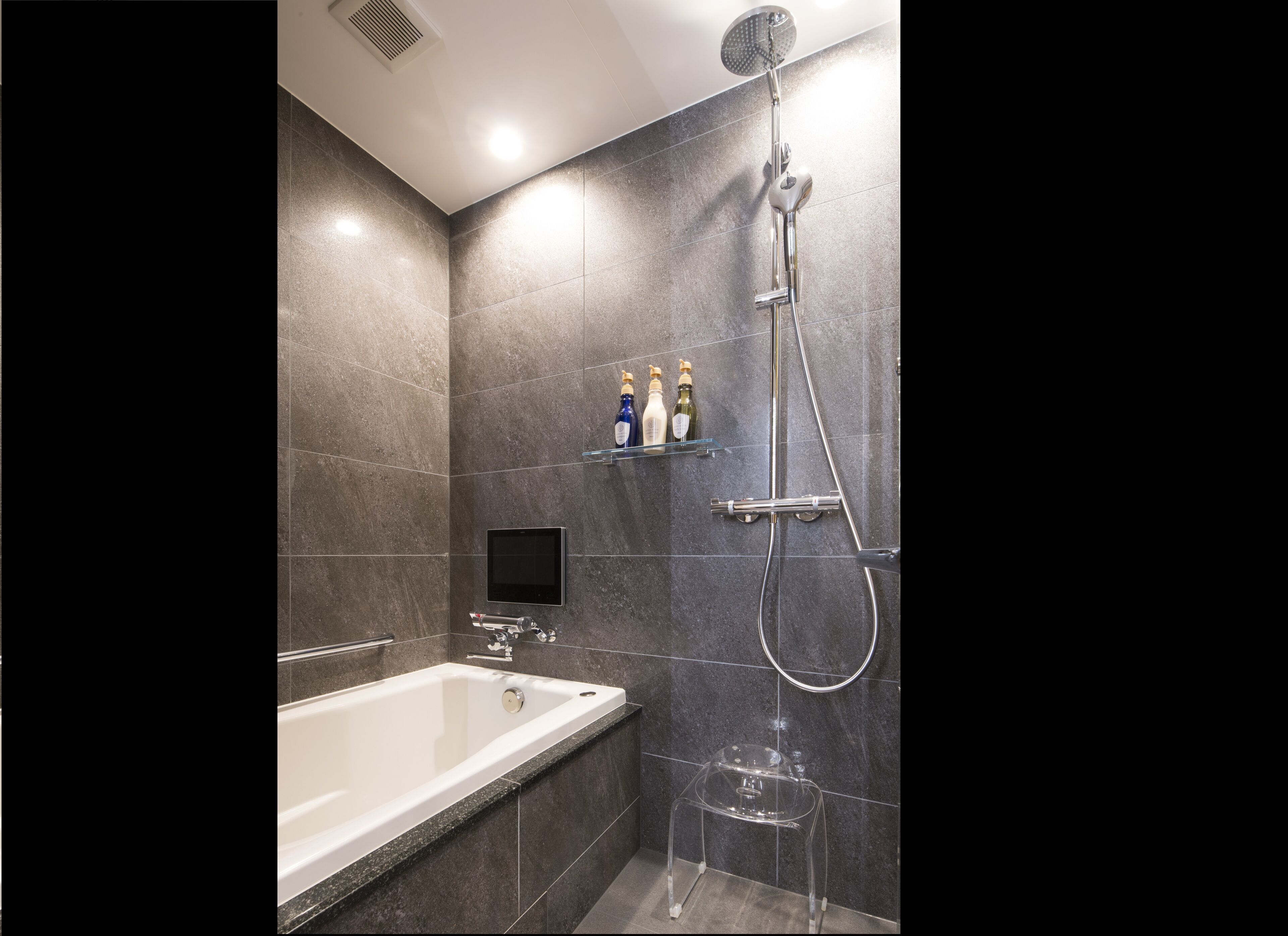A modern bathroom with a bathtub, a shower, and a glass shelf holding toiletries.