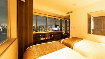 A hotel room with two beds, a desk, and a large window offering a city view.
