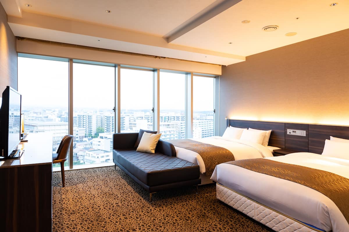 A hotel room with a large window, a sofa, a bed, and a desk.