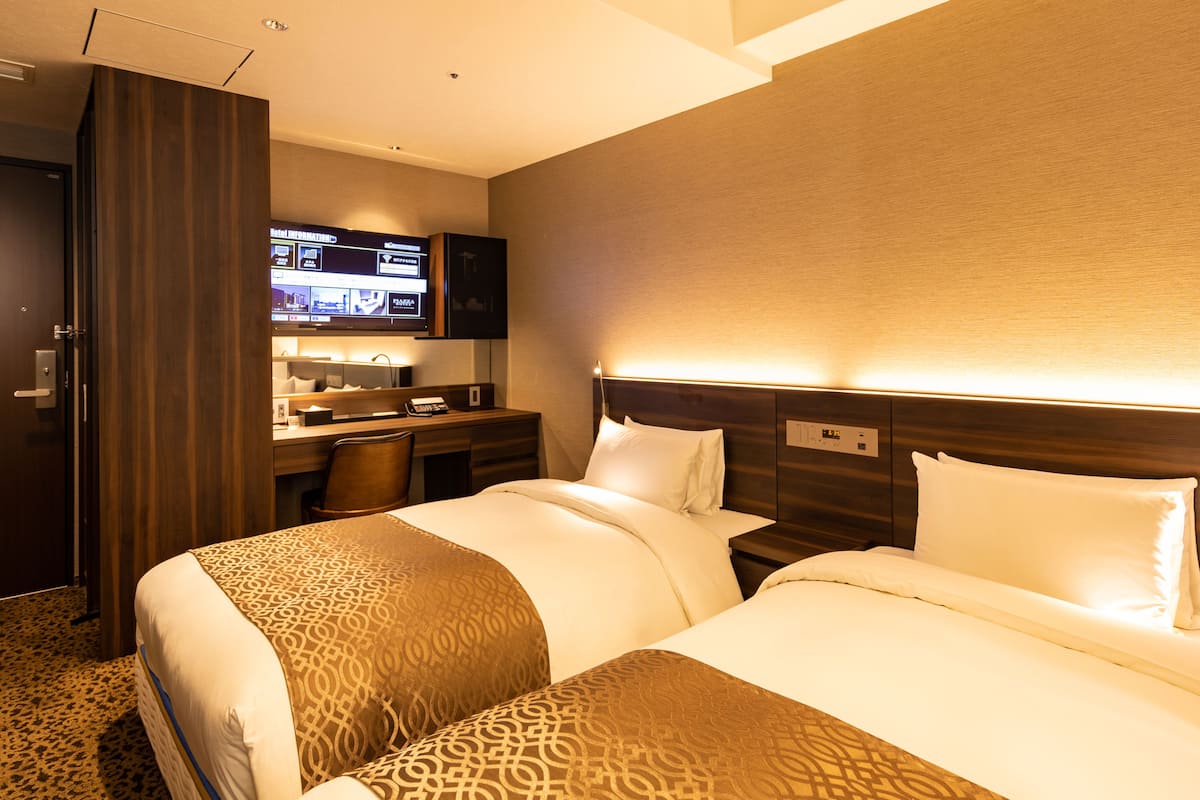 A hotel room with two beds, a desk, a television, and a minibar.