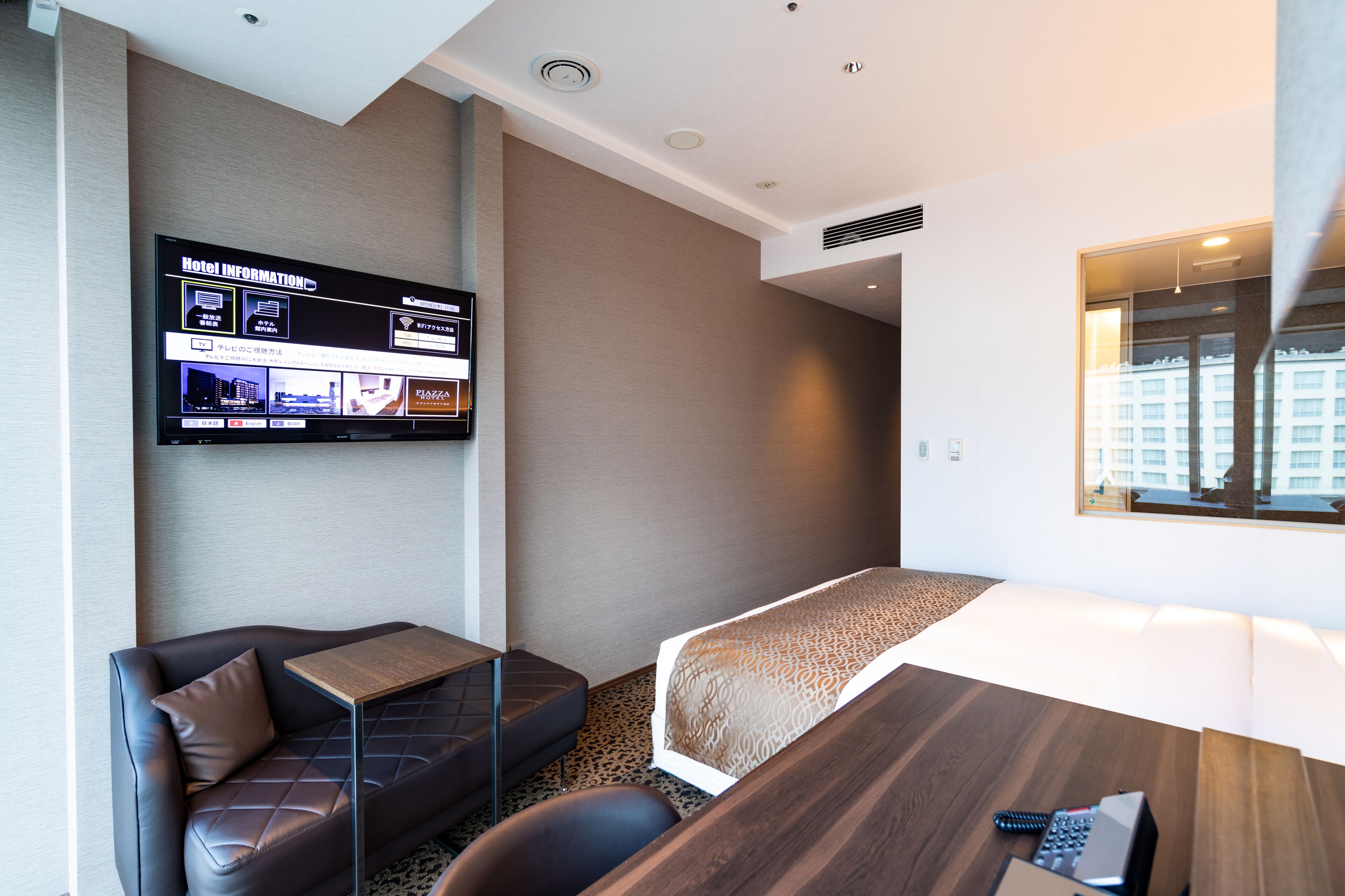 Habitación de hotel con una cama, un pequeño sofá, una mesa de madera y un televisor mostrando información del hotel.