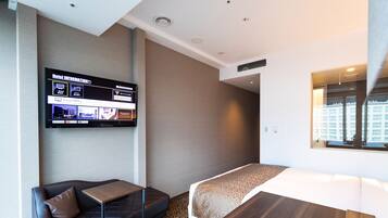 Habitación de hotel con una cama, un pequeño sofá, una mesa de madera y un televisor mostrando información del hotel.