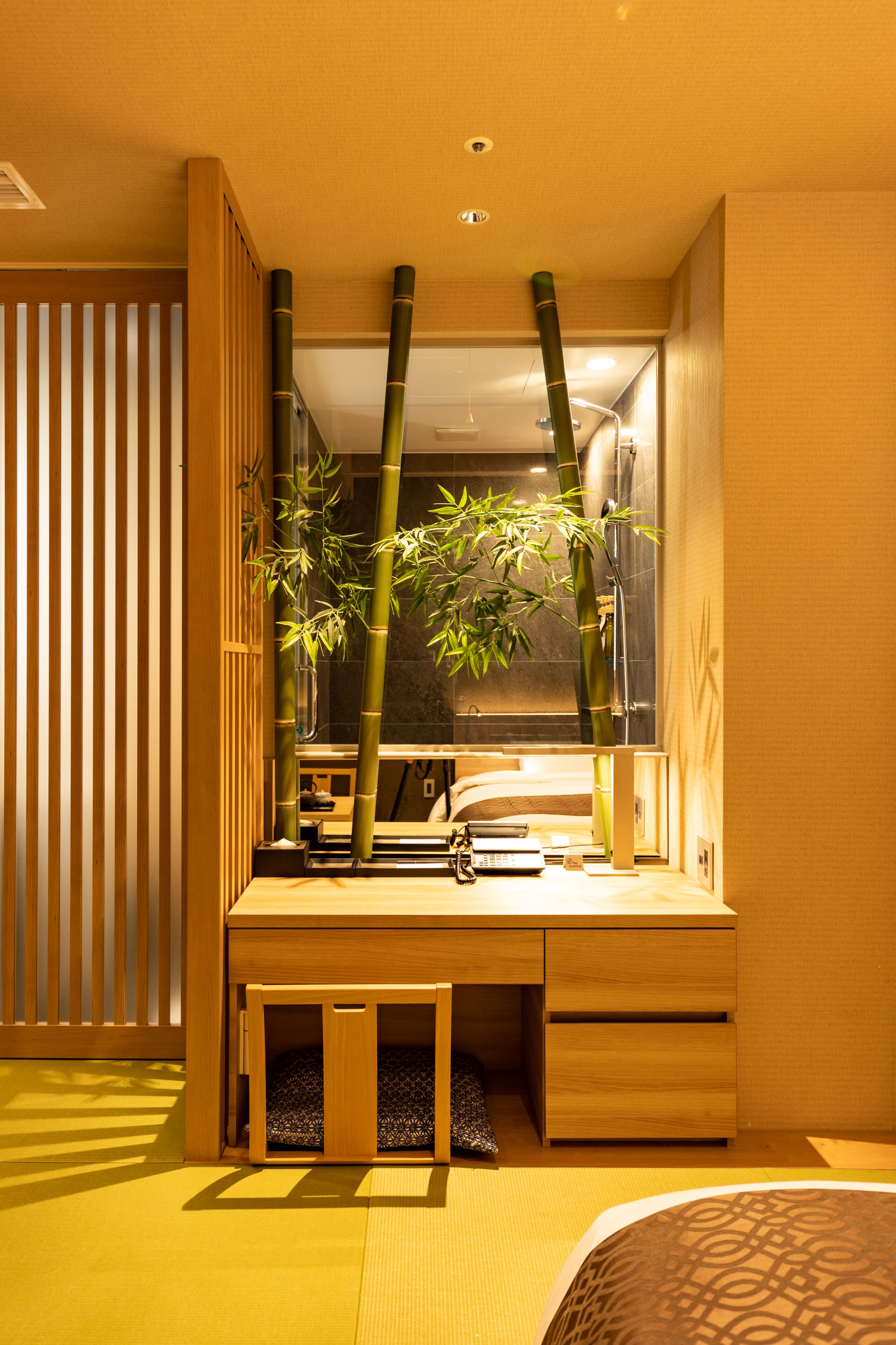 A compact bedroom with a built-in desk, a window with bamboo plants, and a sliding shoji screen.