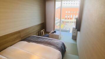 A hotel room with a large bed, a bedside table, a chair, a desk, and a view of the outside.