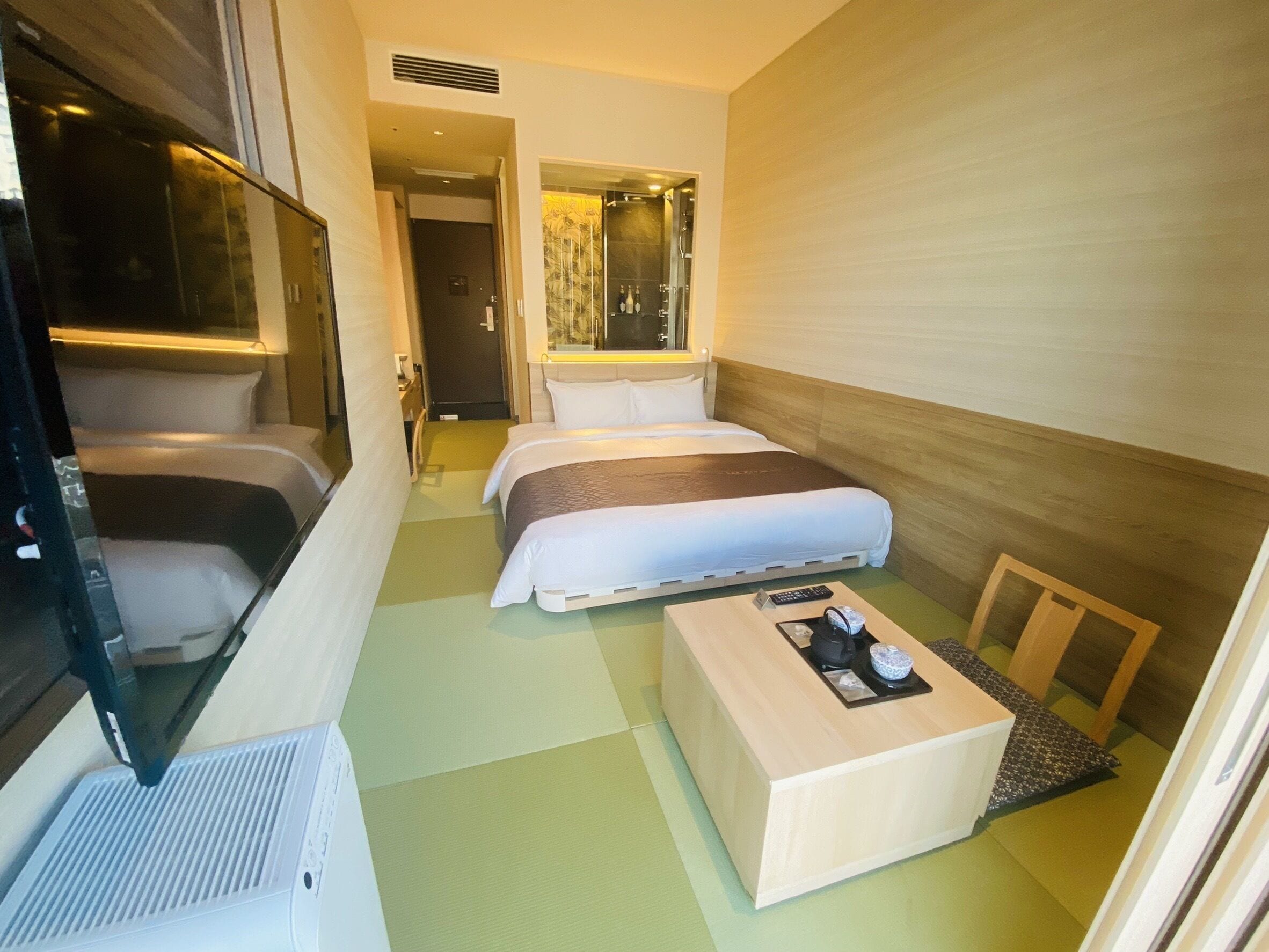Una habitación de hotel con cama, una mesita, una silla y una ventana.