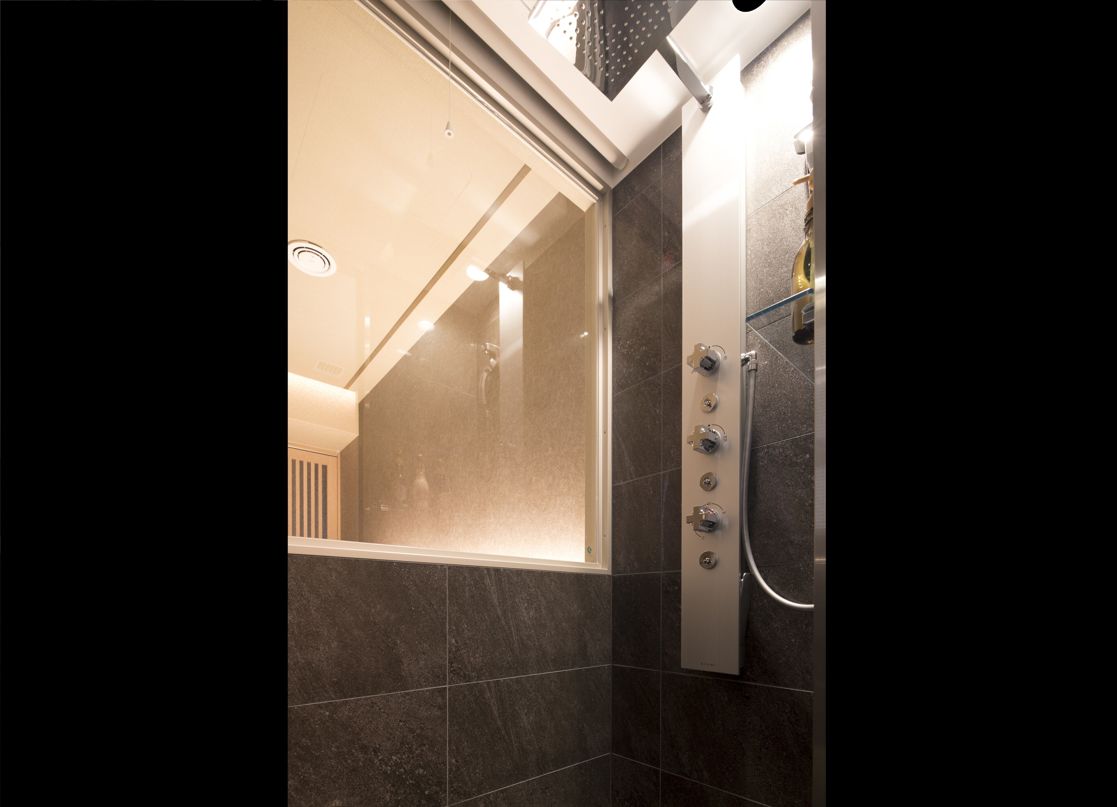 A modern bathroom with a glass shower enclosure, dark tiles, and a visible control panel for the shower.