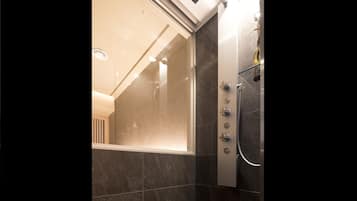 Een moderne badkamer met een glazen douchecabine, donkere tegels en een zichtbaar bedieningspaneel voor de douche.