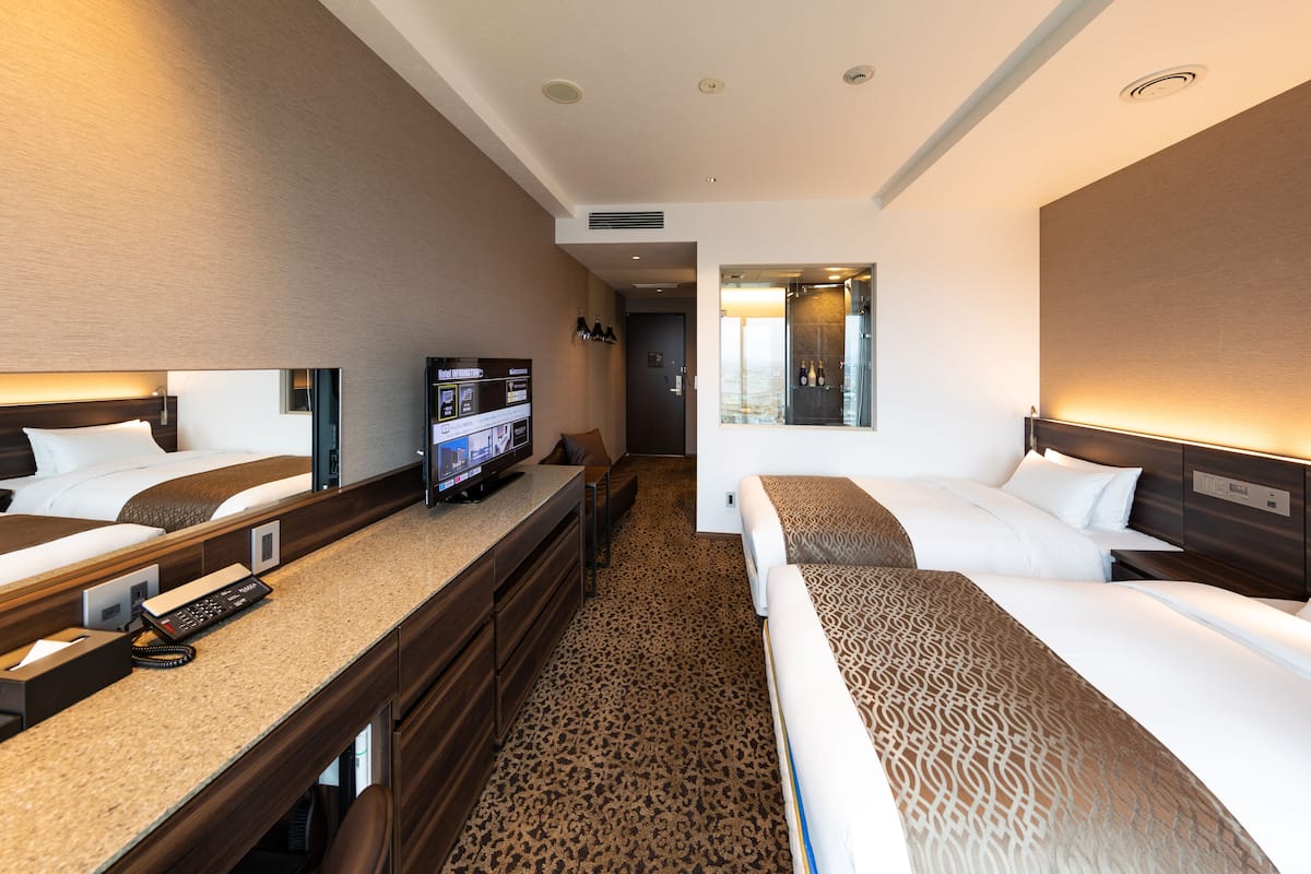 A hotel room with two beds, a desk with a TV, and a mirror.