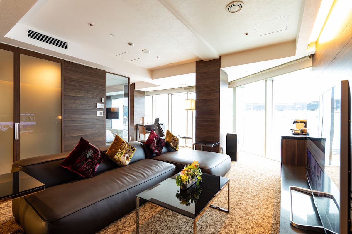 A modern hotel room with a leather sofa, a glass coffee table, and a flat-screen TV.