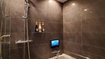 Un baño moderno con ducha de vidrio, bañera independiente y televisor montado.