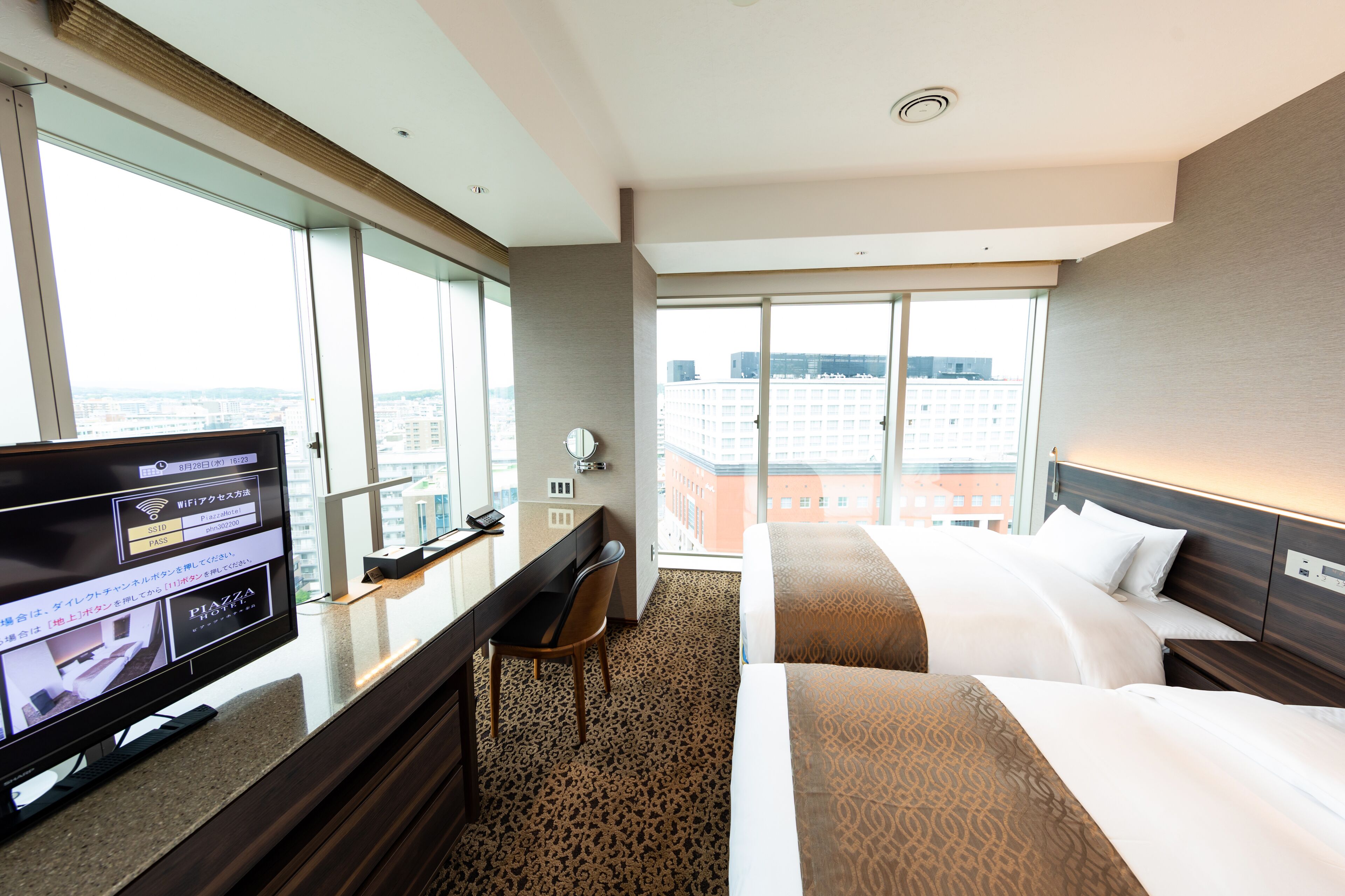 Una habitación de hotel con un ventanal grande, un escritorio con computadora y dos camas.
