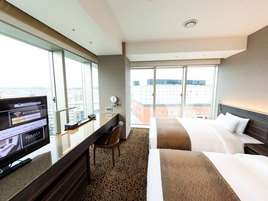 Una habitación de hotel con un ventanal grande, un escritorio con computadora y dos camas.