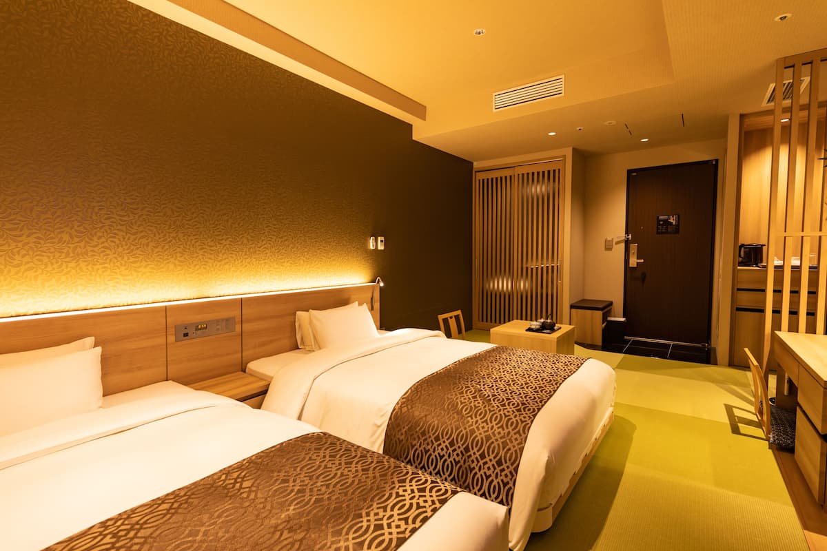 A hotel room with two beds, a desk, a chair, and a wardrobe.