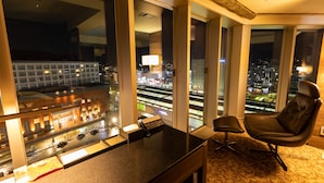 A modern hotel room with large windows offering a city view, a desk with a phone, and a comfortable chair. - Piazza Hotel Nara (Nara)