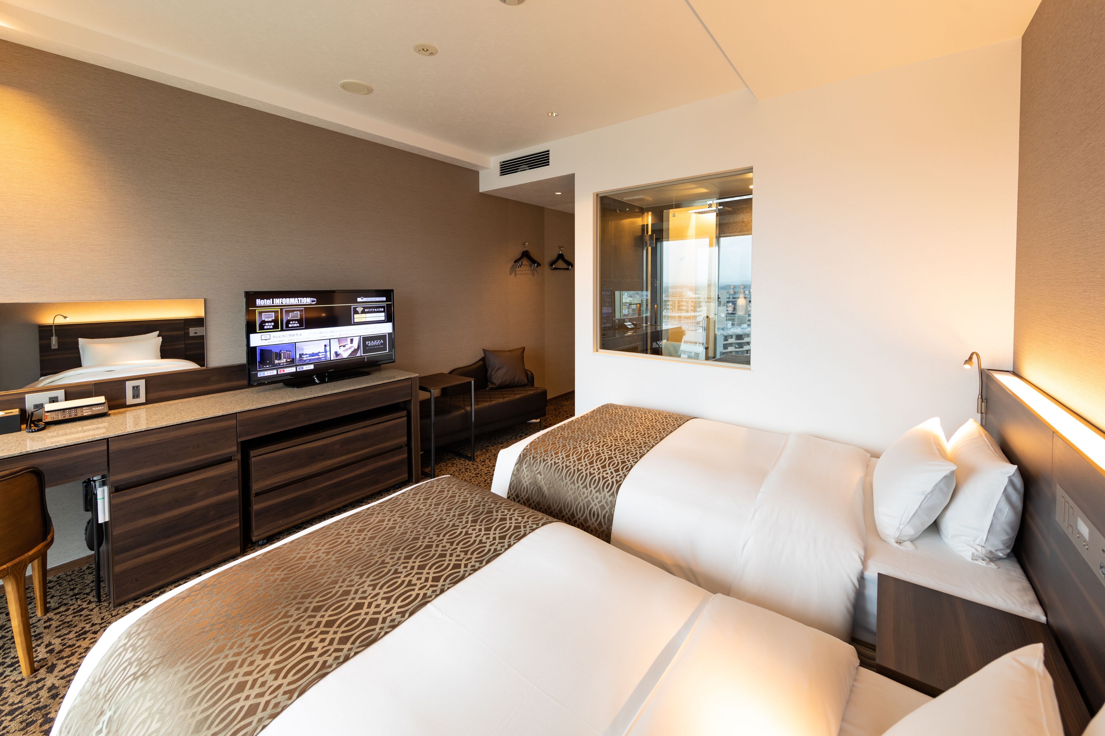 Ein Hotelzimmer mit Bett, Schreibtisch, Fernseher und einem Fenster mit Blick auf die Stadt.