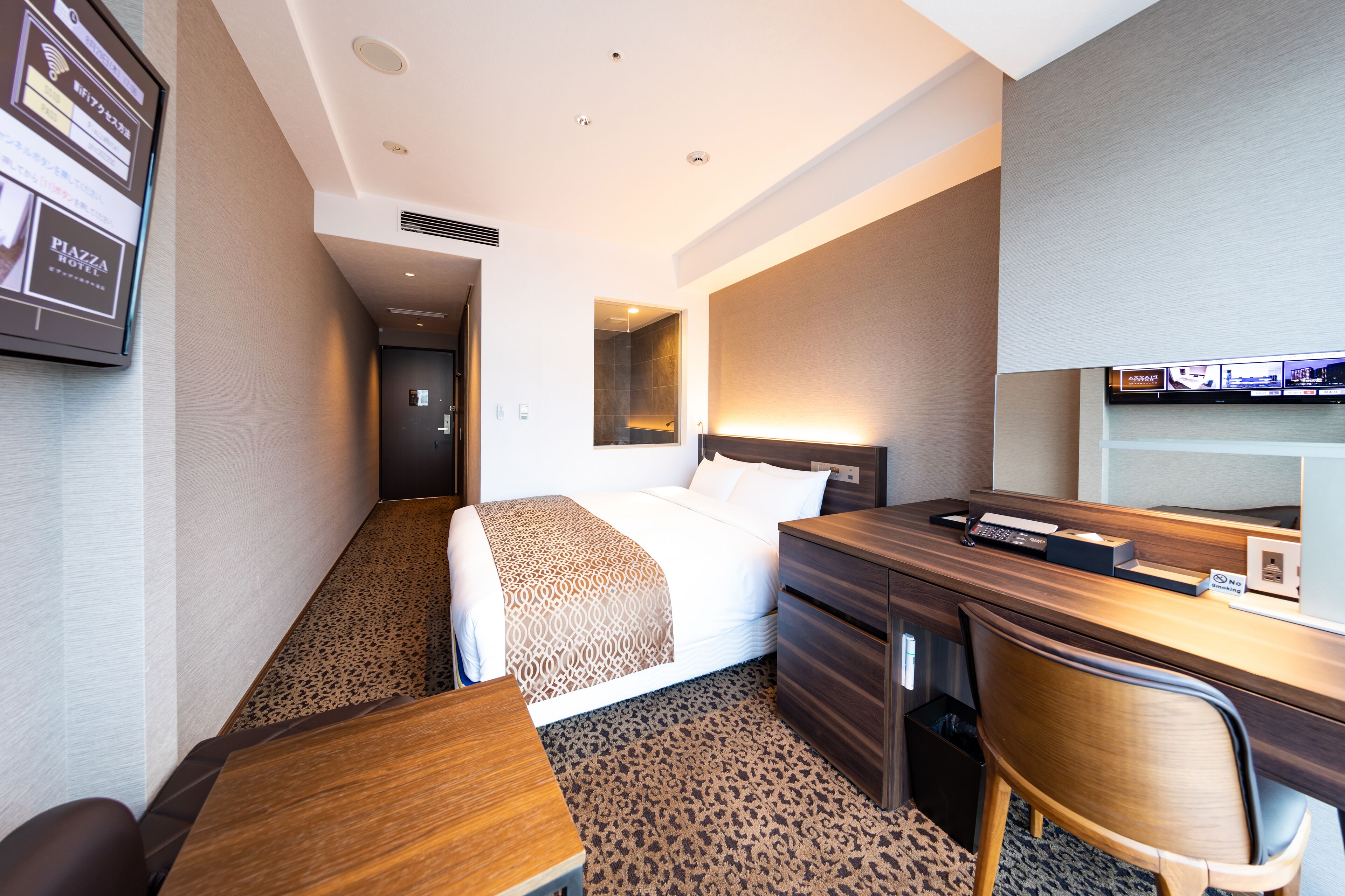 A hotel room with a bed, desk, chair, and a TV mounted on the wall.