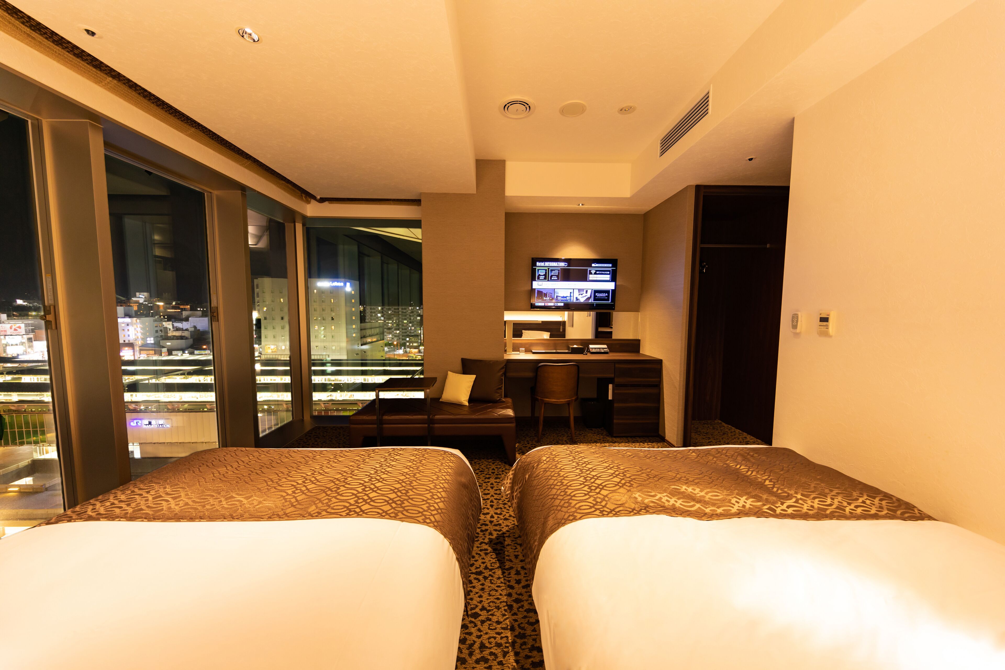 Ein Hotelzimmer mit zwei Betten, einem Schreibtisch, einem Fernseher und Blick auf die Stadt.