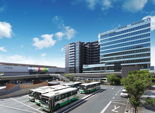 A modern hotel with a glass facade, a parking lot with buses, and a train station in the background. - Piazza Hotel Nara (Nara)