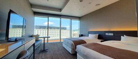 Habitación de hotel con una cama grande, un escritorio con una silla, televisión y vista a la ciudad a través de amplias ventanas.