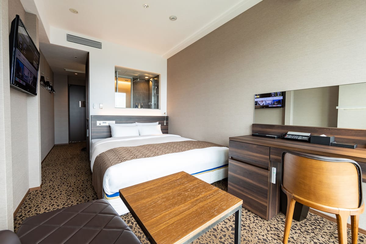 A hotel room with a bed, a desk, a chair, a TV, and a mirror.