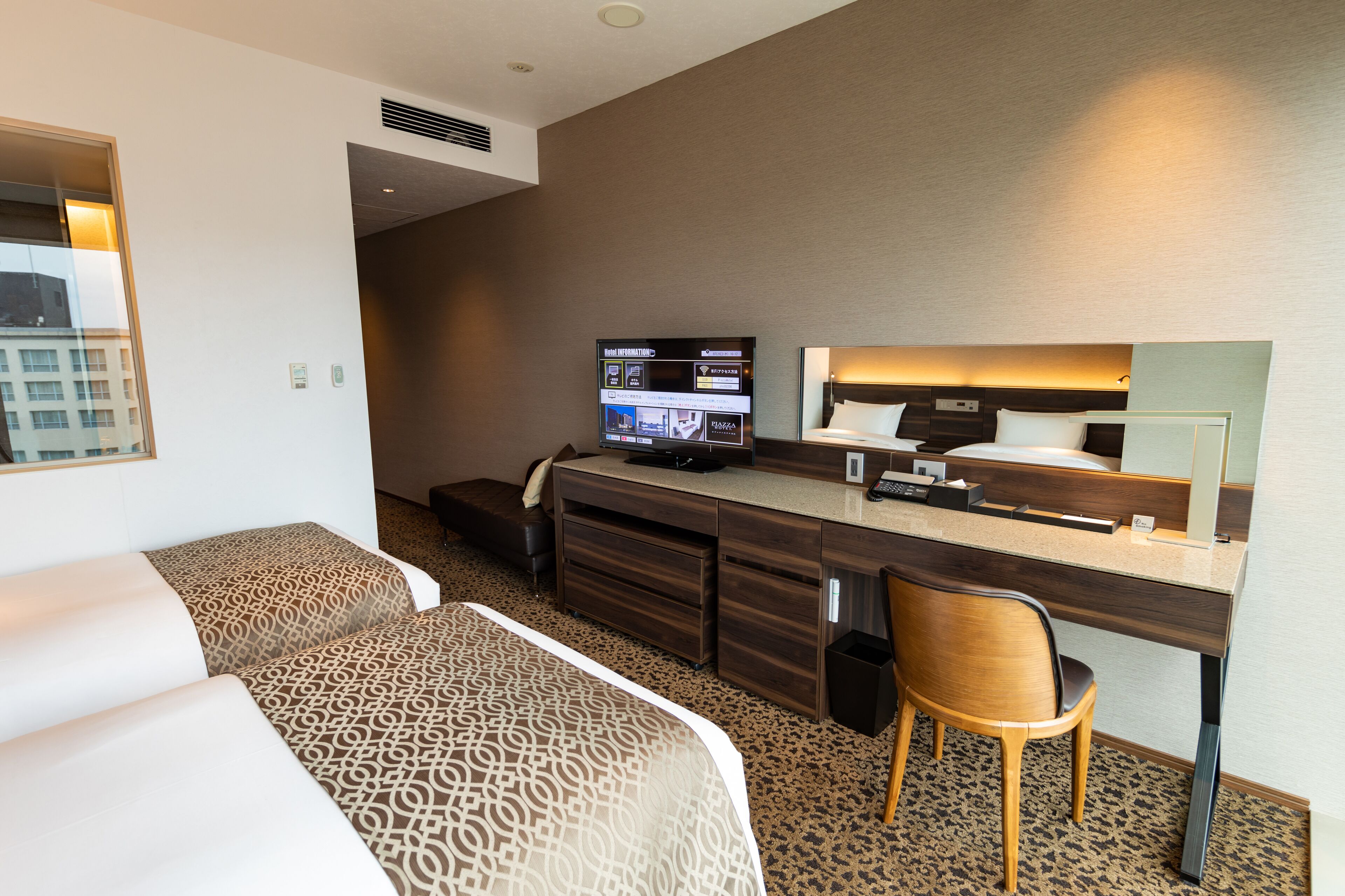 A hotel room with two beds, a desk with a computer, a chair, and a large mirror.