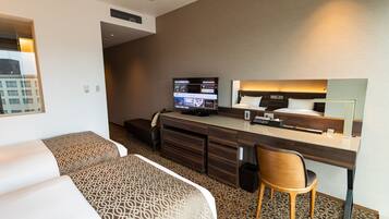 A hotel room with two beds, a desk with a computer, a chair, and a large mirror.