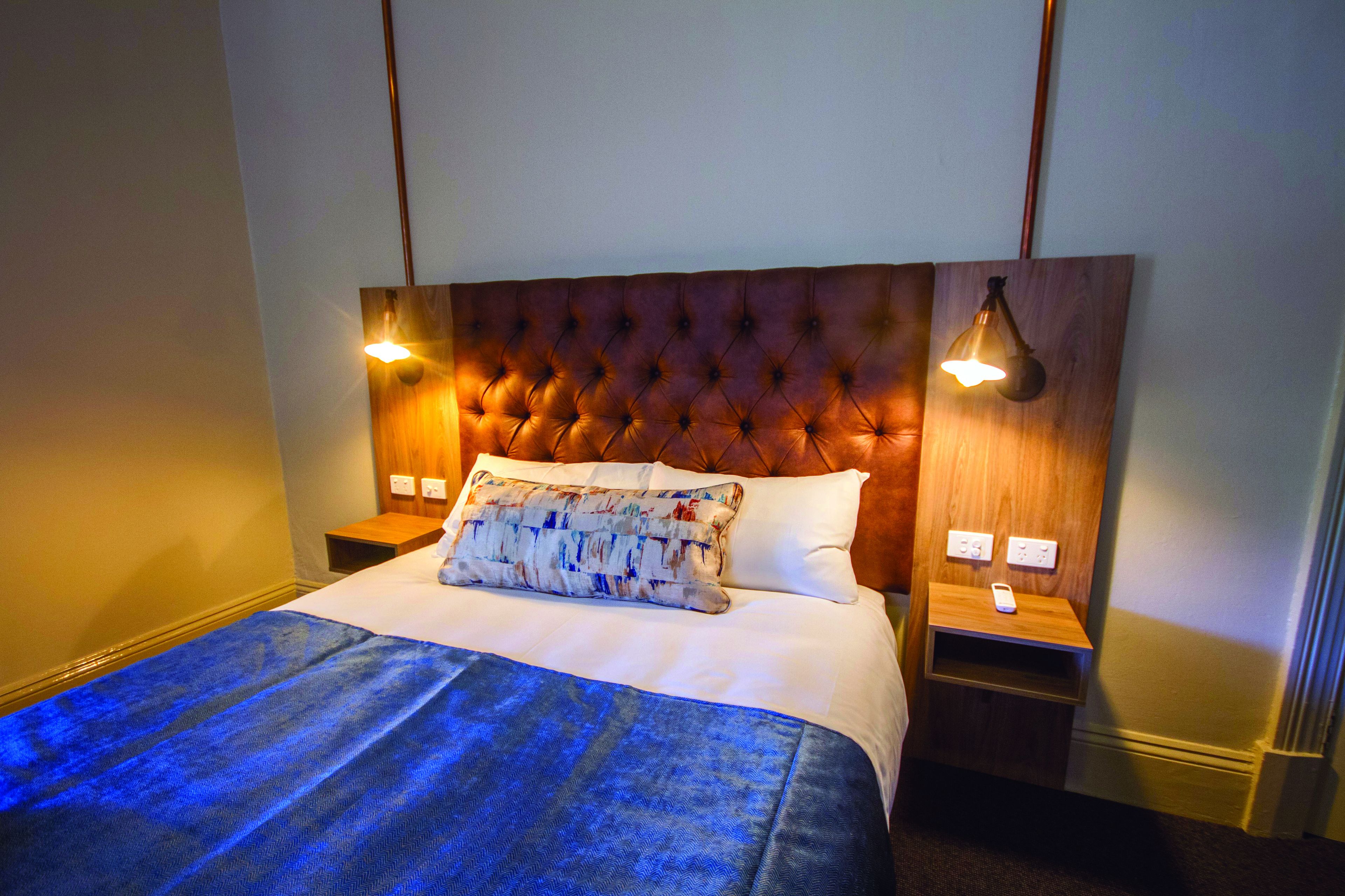 A neatly made bed with a tufted headboard, two bedside lamps, and a bedside table with a remote control.