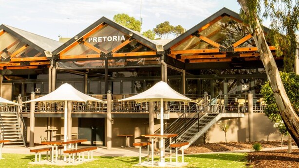 A modern building with the name 'Pretoria' on the facade, featuring outdoor seating areas with umbrellas and benches. - Pretoria Hotel (Mannum)