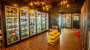A bar area with multiple refrigerators stocked with beverages, wooden flooring, and hanging light fixtures. - Pretoria Hotel (Mannum)