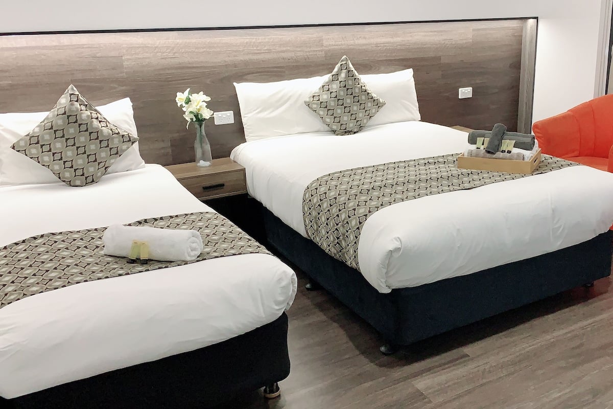 Ein Hotelzimmer mit zwei Betten, einem Nachttisch, einer Vase mit Blumen und einem orangefarbenen Sessel.