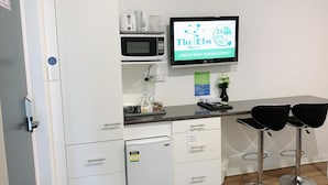 A kitchenette with a microwave, coffee maker, and a TV displaying 'The Elm Motel' sign. - Elm Motel (Golden Square)