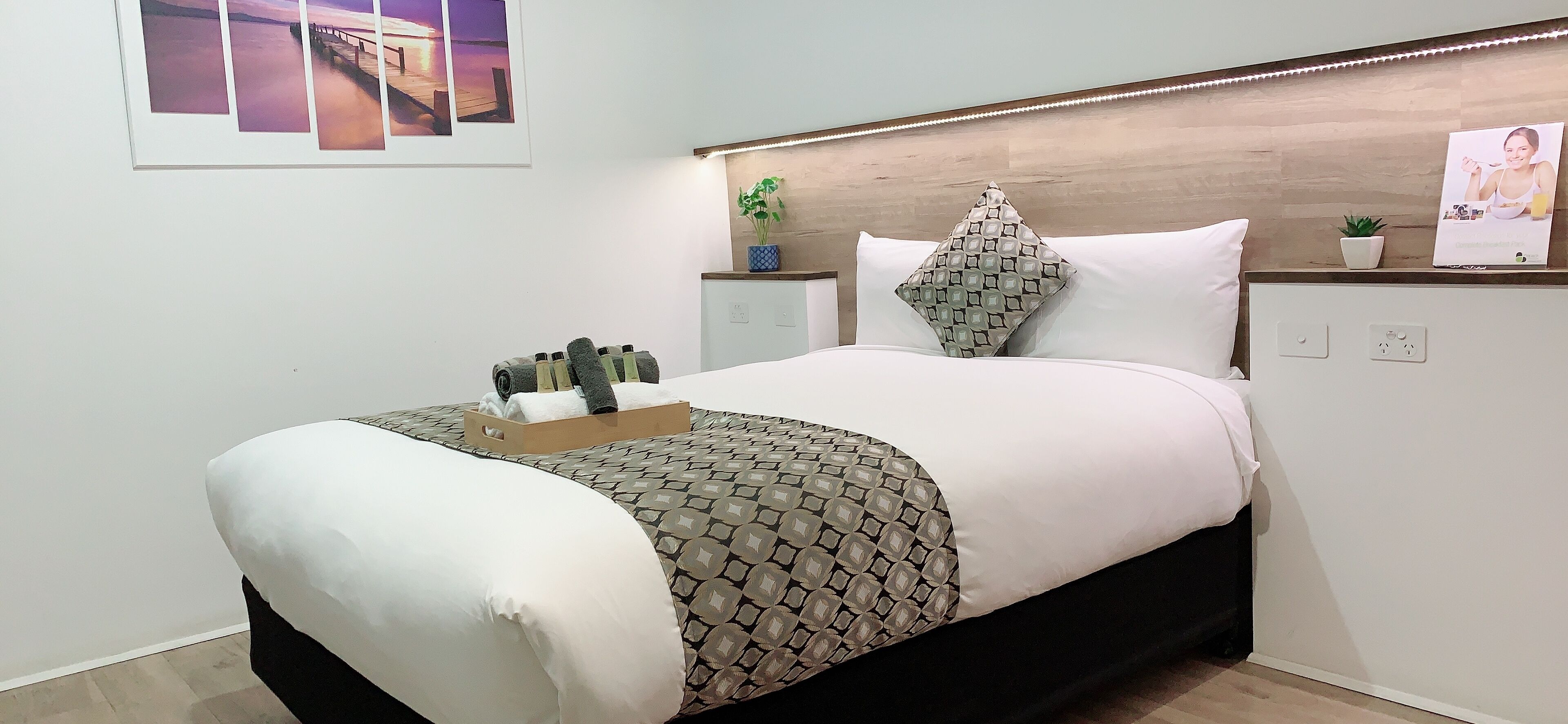 A neatly made bed with a patterned bedspread, a pillow, and a tray of toiletries.